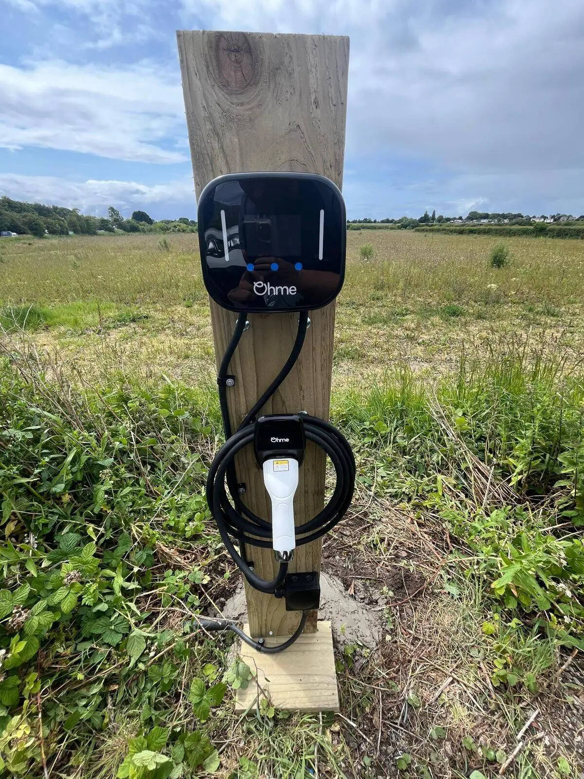 Ohme Home Pro charger mounted on a timber support in a countryside setting